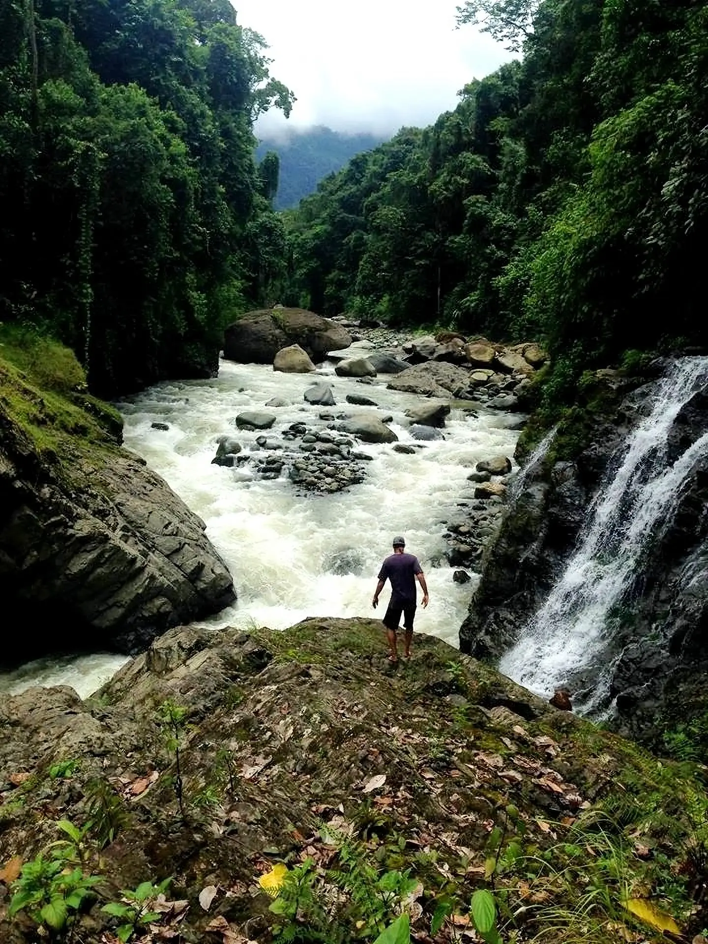 A guest at the river below a rainforest waterfall near Posada Natura