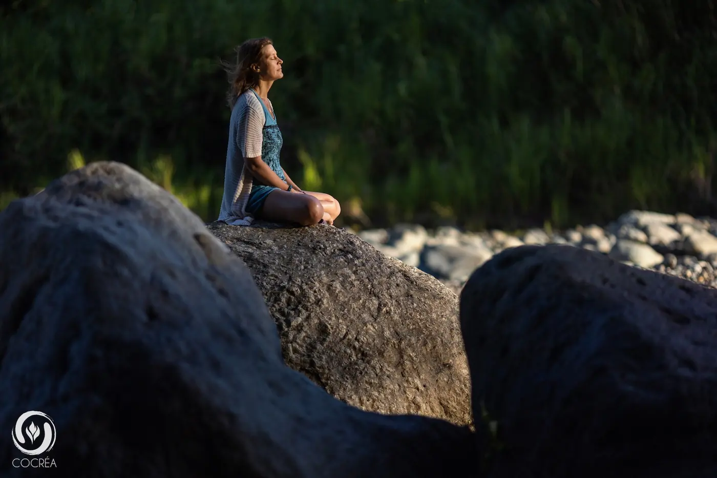 A guest meditating on a river boulder at dusk